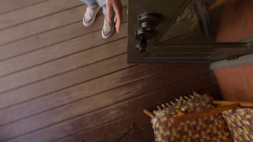 Camera at the door overhead view of a woman opening it and stepping out