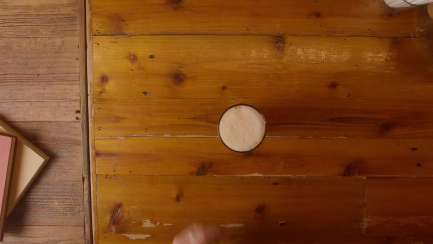 A human hand places a glass of drink on the table and another hand picks up the glass