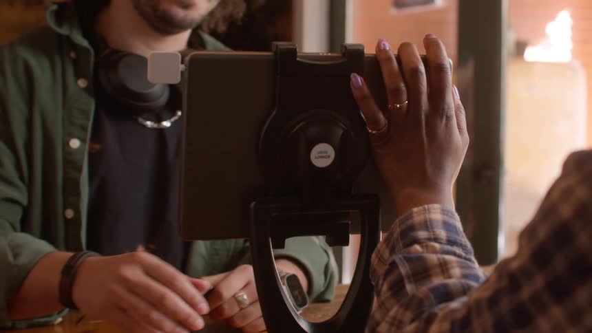 A barista swiping a card and turning a tablet for a young man to pay