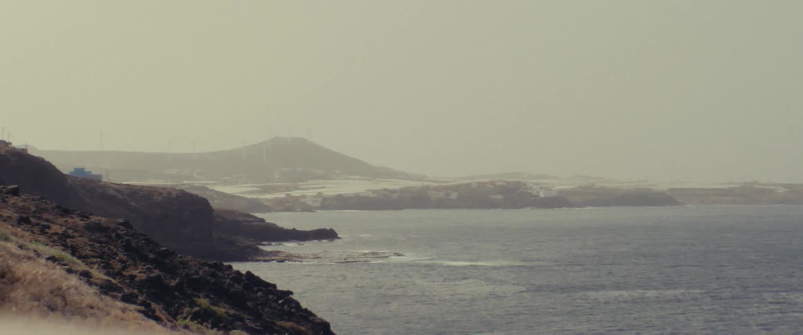 Rocky sloped coastline and sea with fog and mountains in the background