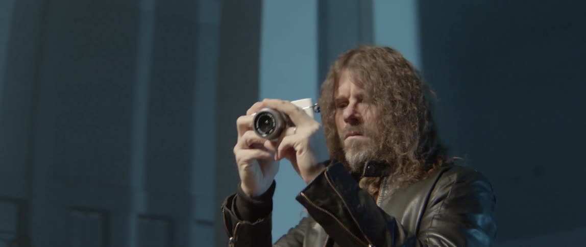 Long haired man in leather looks through a digital camera
