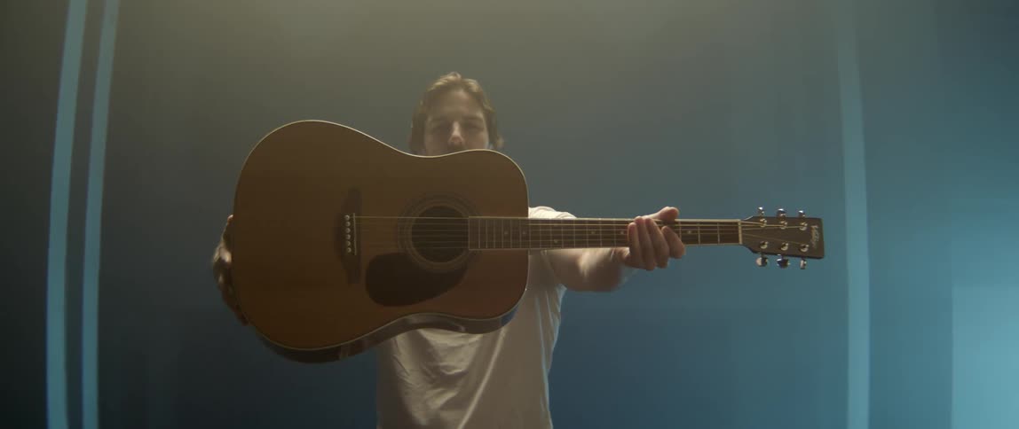 Creative portrait of a male musician holding his acoustic guitar in a studio environment.