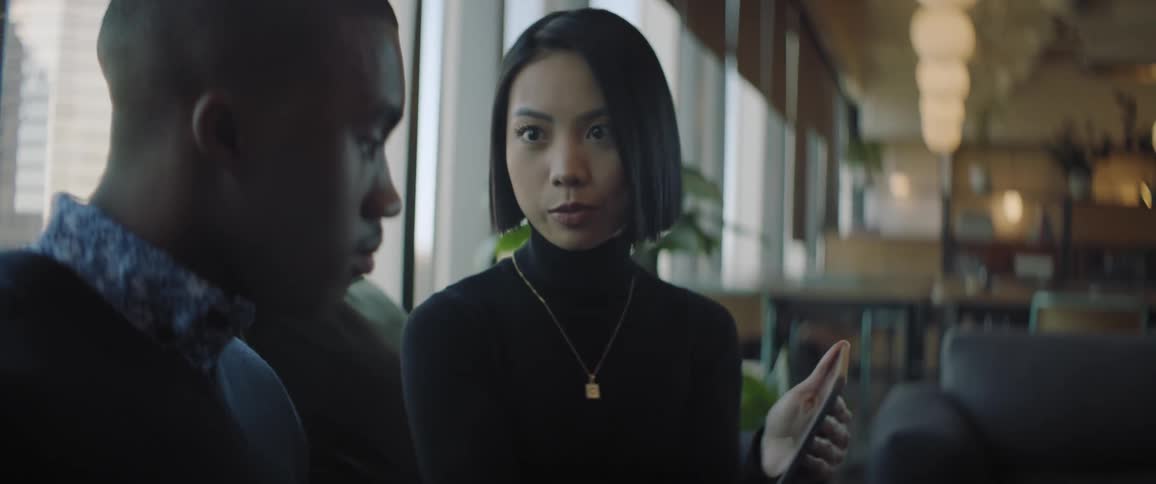 A young woman and a man are sitting and talking while she holds a tablet