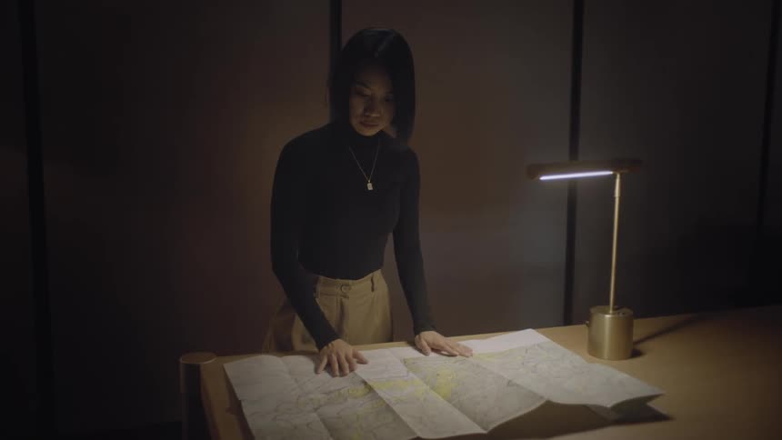 A young asian woman studies a map under a desk lamp in an office