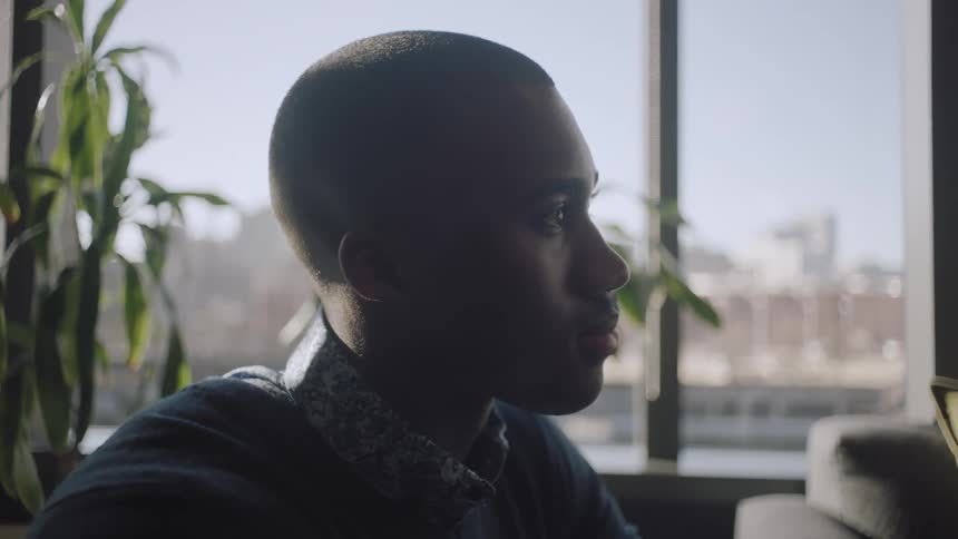 Black man sits in office near window and plant