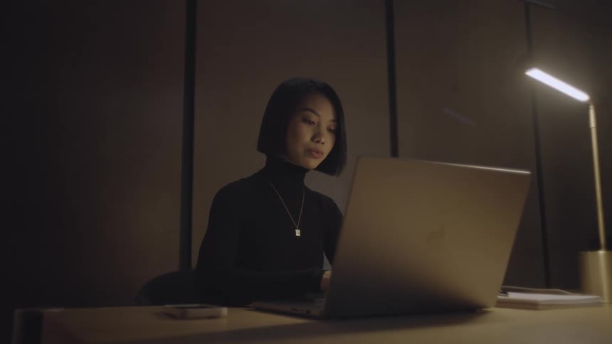 A young woman sits at her open laptop while typing on its keyboard