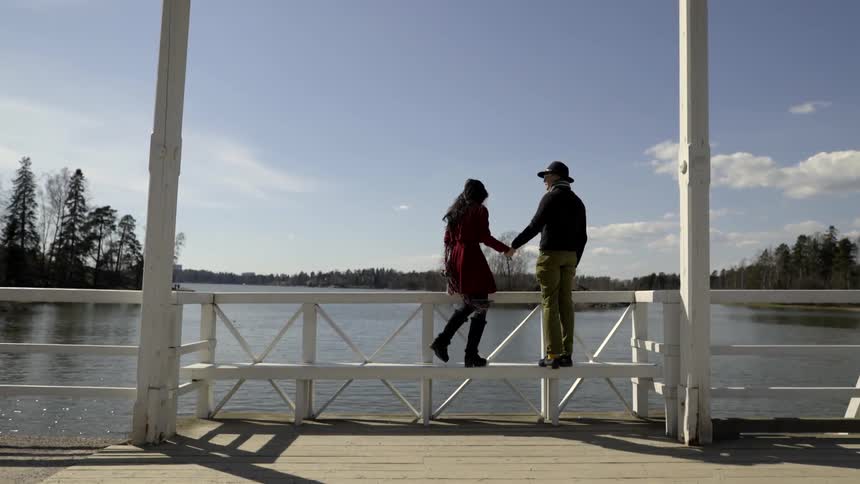 A man and woman climb up on a bench near a lake and embrace