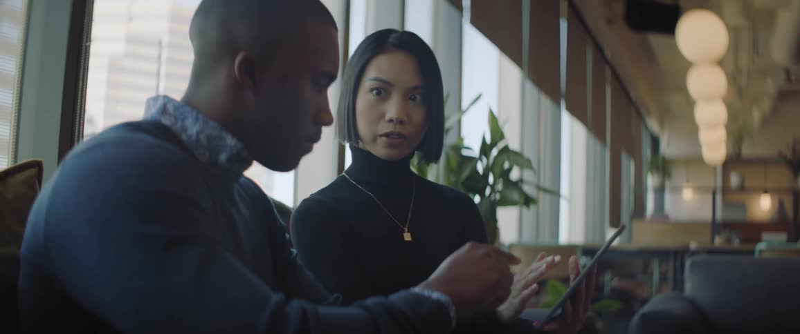 Man and woman talking indoor while holding a tablet computer in a seated position