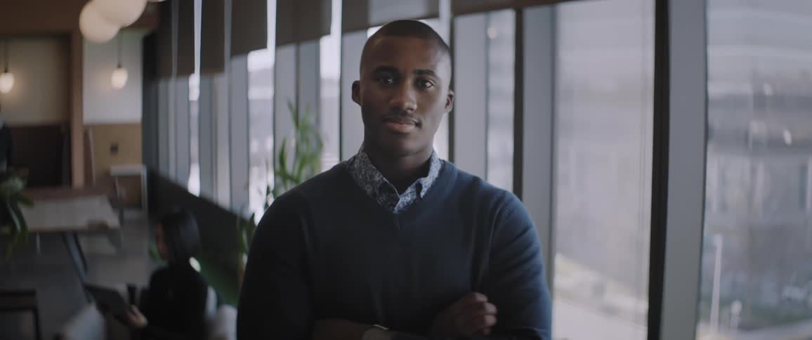 Businessman wearing a blue shirt stands with arms crossed in the office