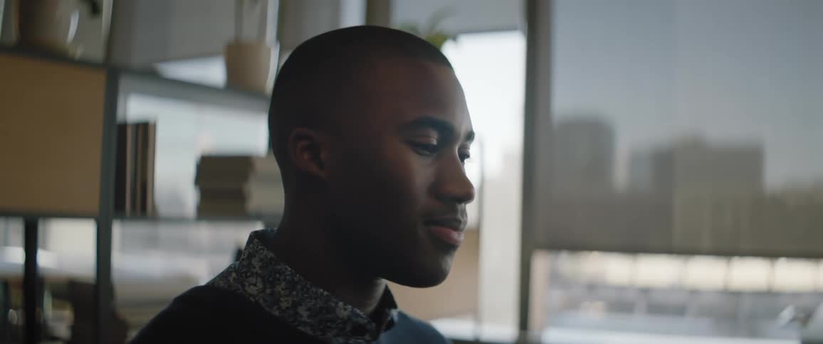 Young black adult male in an office building looking down and nodding with natural light coming through the window in the background