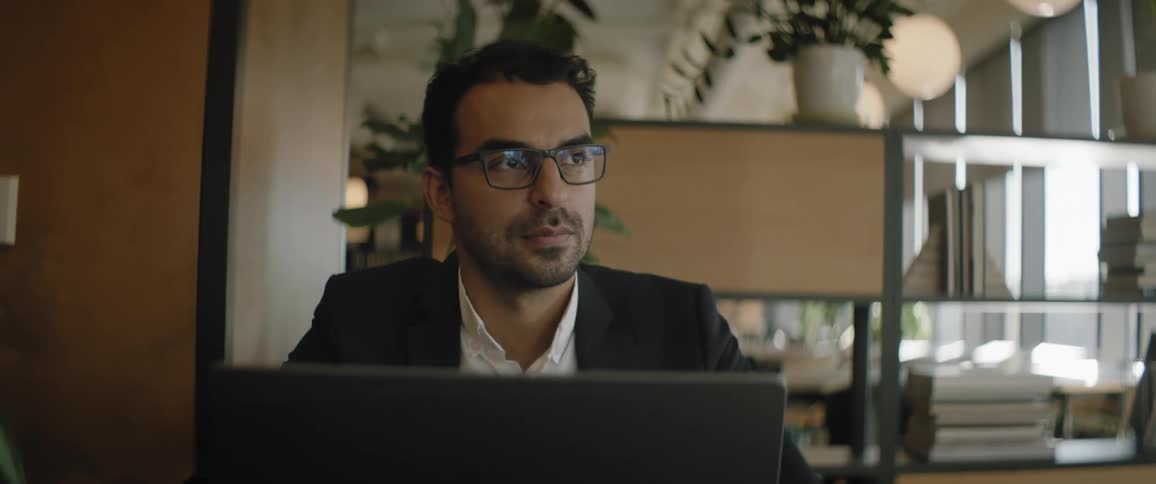 Man sitting in office in front of computer looks up in thought