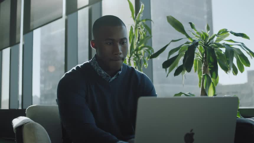 A man is sitting in the office typing on a laptop