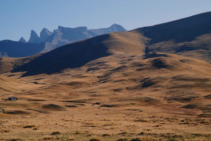 Grasslands over dark hills next to majestic mountains under a clear sky