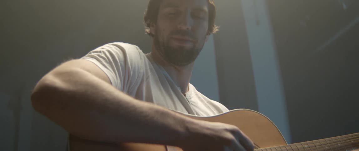 A young man playing a wooden acoustic guitar while performing in a professional setting
