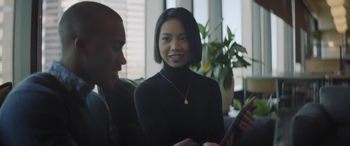 Asian woman and black man sit in office having a conversation near window
