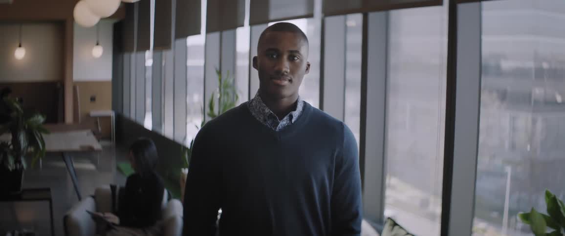 Black man wearing sweater stands near window indoors office