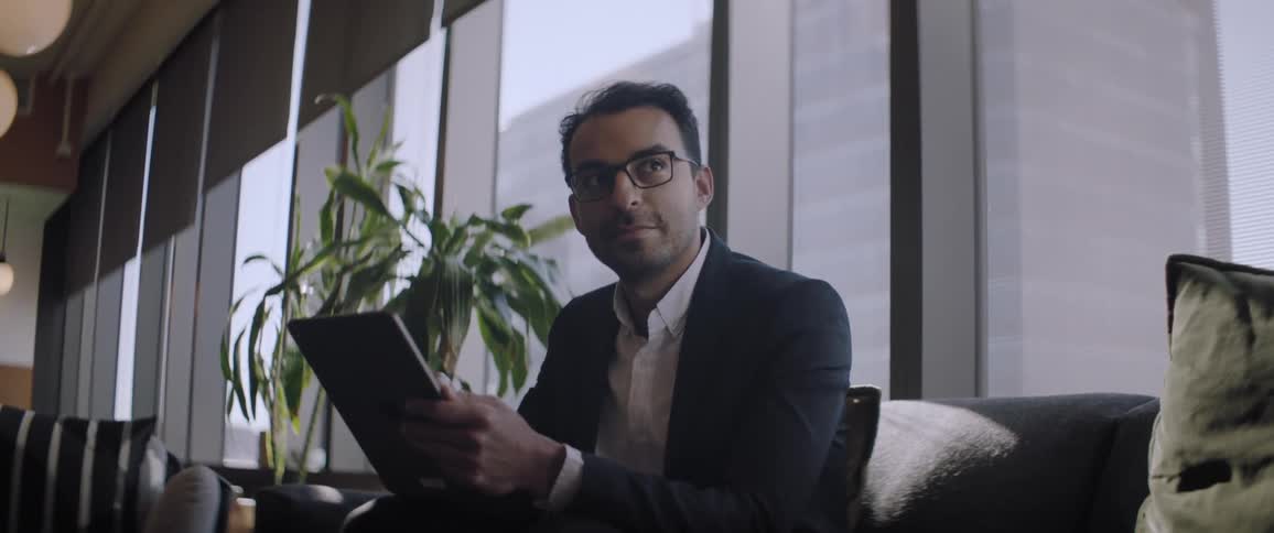 A man putting on a suit is sitting on the chair and operating his tablet