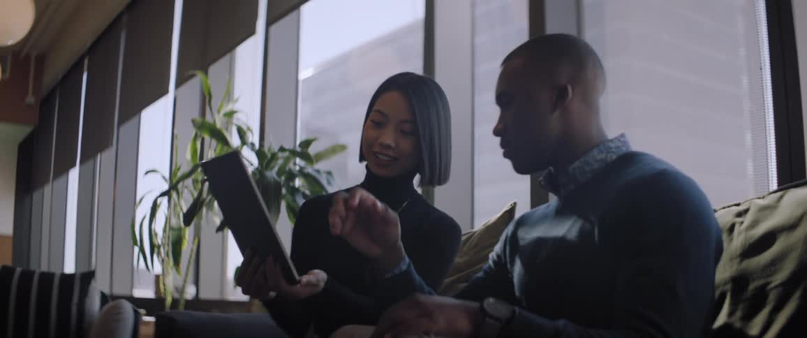 A woman and a man sitting are talking and looking at a tablet that is in the womans hand