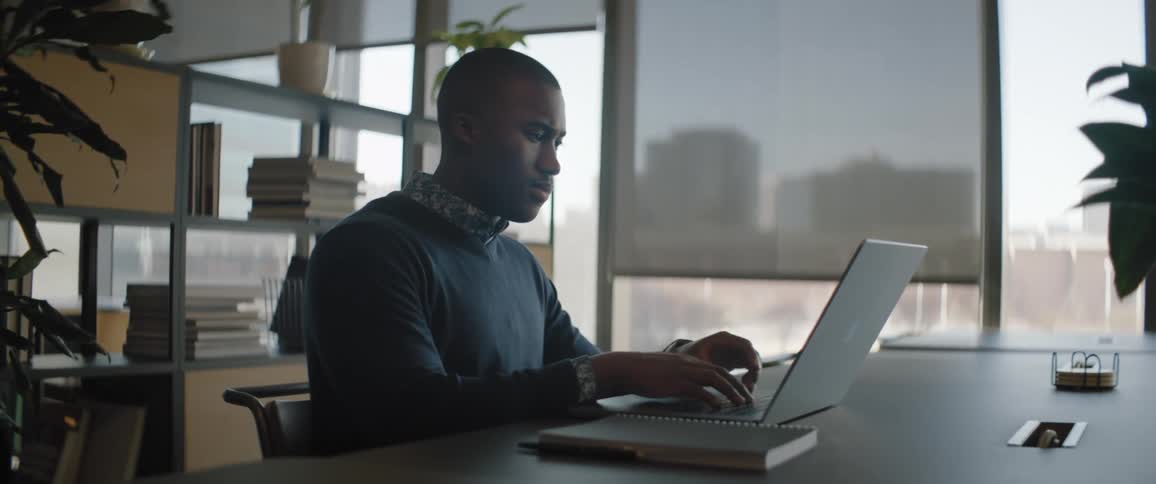 Black man sits at desk in office working on laptop