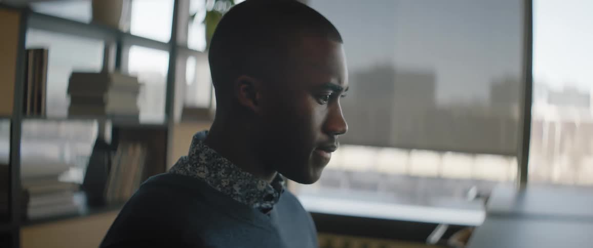 Black man sits indoors in office near window