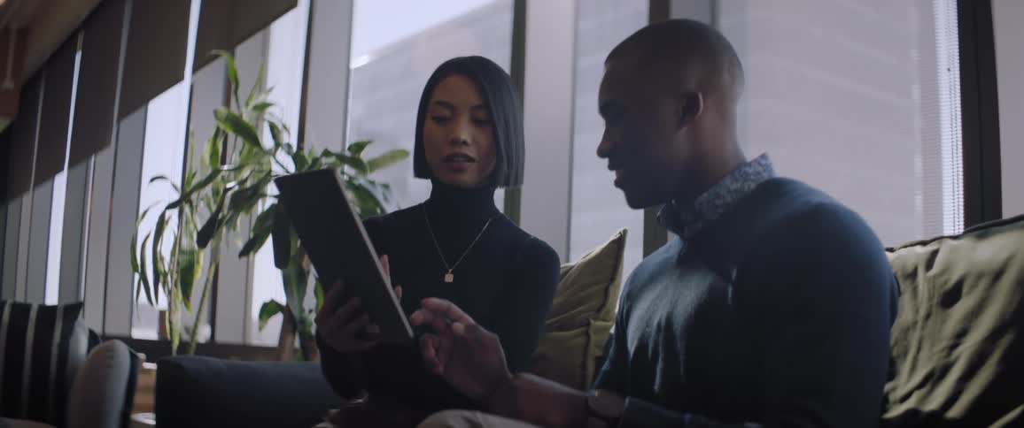 A man and a woman are sitting on a sofa and looking at a tablet and talking