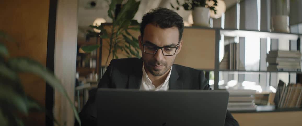 A man putting on a suit and an eye glass operating his laptop in his office