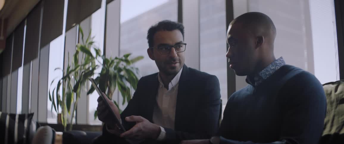 Two men looking at a tablet discussing business in a downtown office building with a lot of windows on a bright day