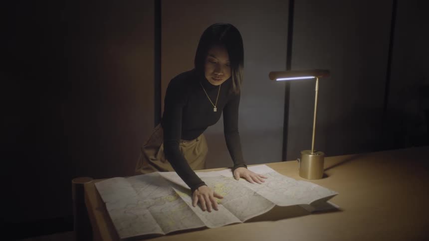A young asian woman studies a map that is lying on a desk in an office area