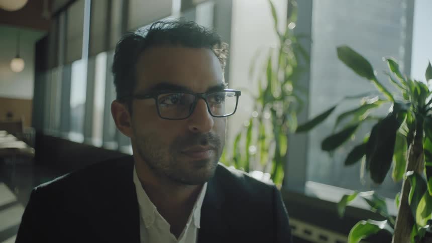 A man wearing glasses sits in an office and looks off in the distance