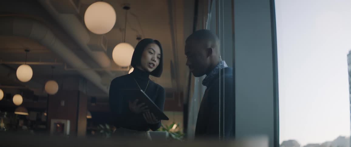 A woman and a man standing are talking and looking at a tablet that is in the womans hand