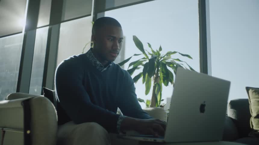 A young man is sitting in an armchair and using a laptop in front of him