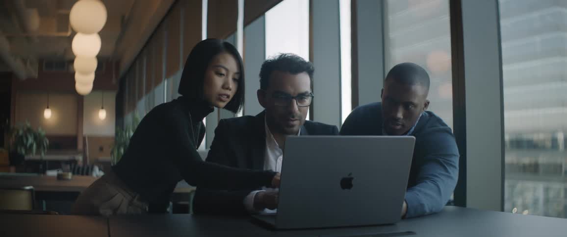 A client sits in the middle of two employees while they look at a laptop screen together