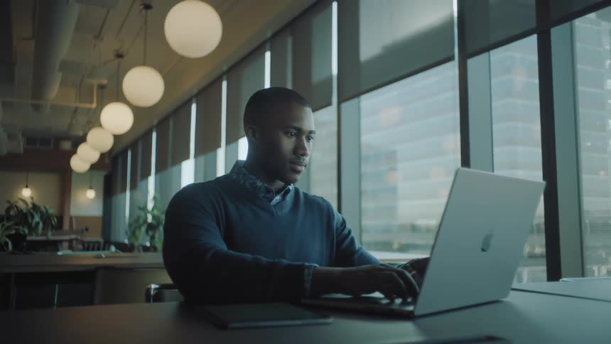 A man is sitting and using a laptop on the table