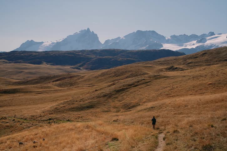 An adult walks down a trail in a wilderness area of hills and mountains