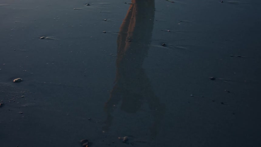A reflection of a person stretching on a wet sand surface
