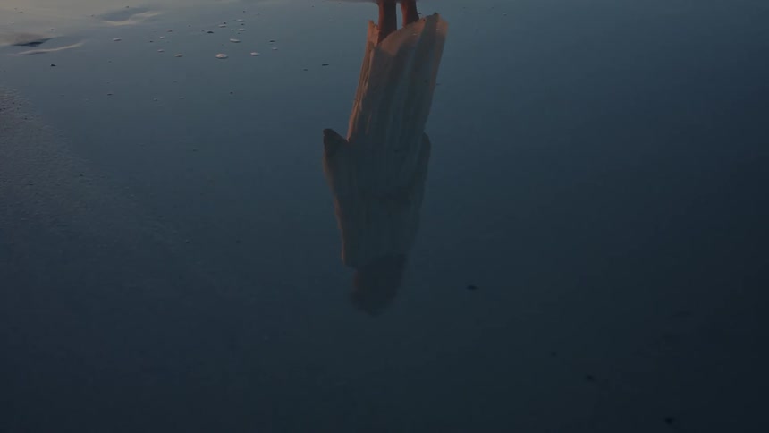 A womans reflection is in the beach water