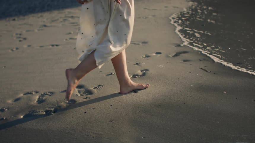 A person walking barefoot along the beach in the morning