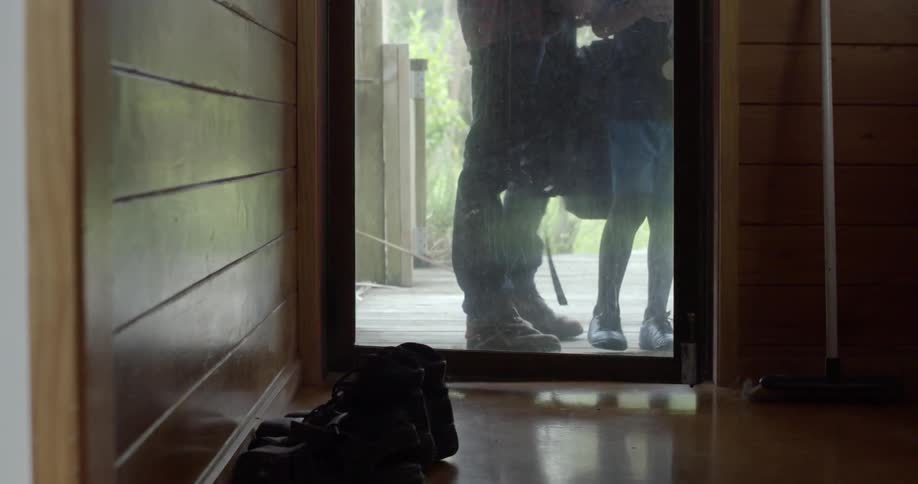 A boy with a medal and a soccer ball walks into a house followed by an adult