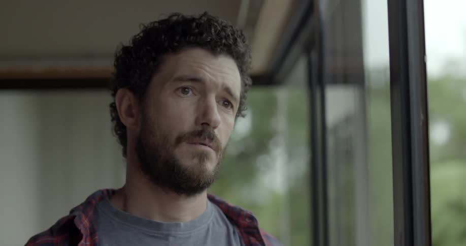 A man stands in a room filled with windows and looks outside