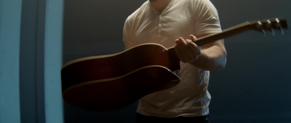 A musician in a white shirt inspecting his guitar in a professional creative environment.