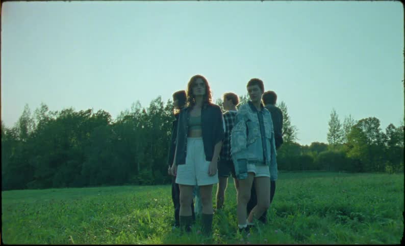 A group of teenagers stand in a circle in the grass