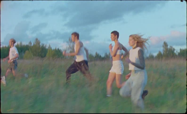 A group of friends running in a meadow during sunset