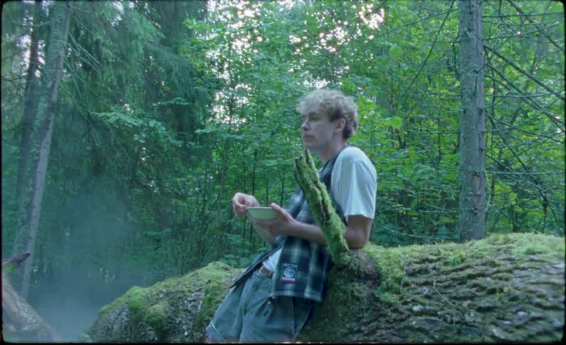 A boy eating in the forest around the campfire