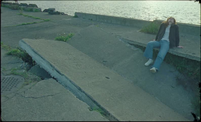 Young blonde woman sits on a broken concrete slab near a river