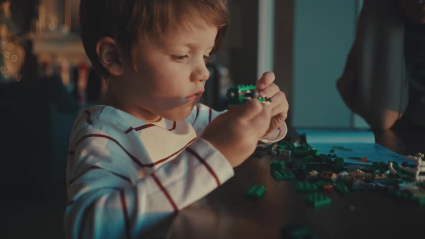 A little boy assembling lego pieces on the wooden table