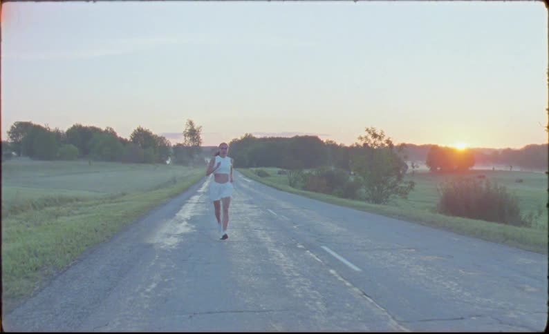 A woman is running on a quiet rural road as the sun sets in the distance