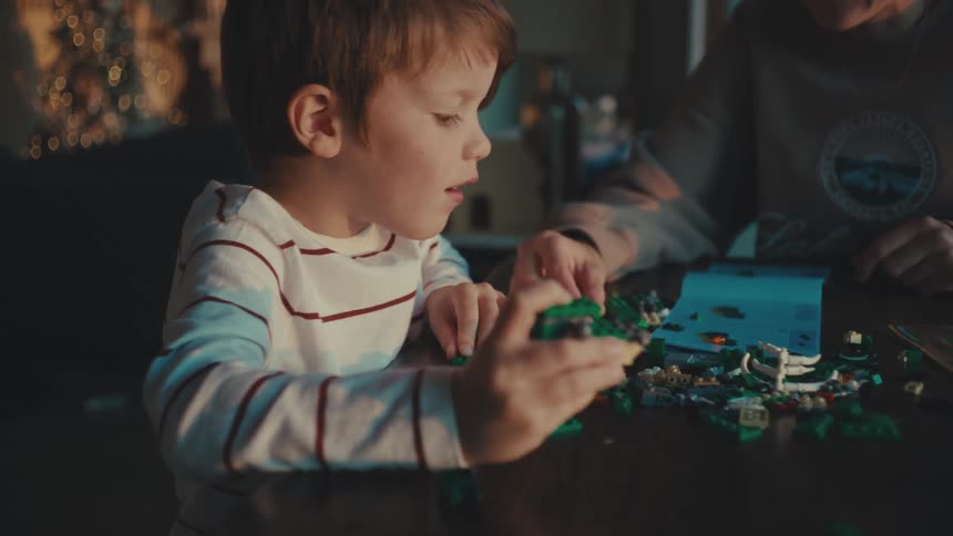 A boy assembling lego pieces on a table during sunset