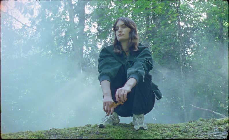 Young woman sits over a fallen tree in the forest caught on vintage film