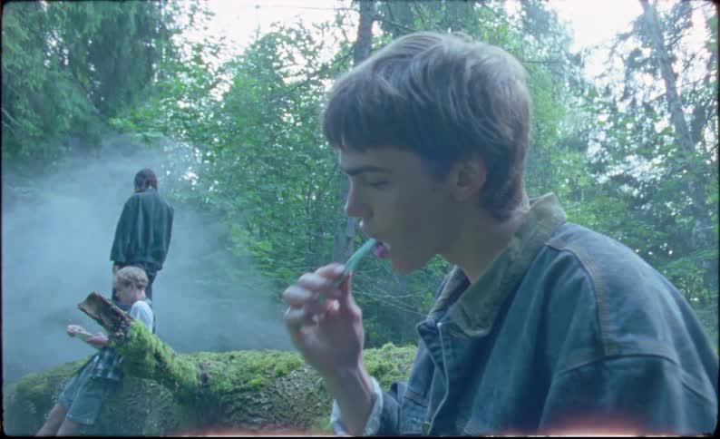 Youth brushes his teeth while camping in woods on a hazy day