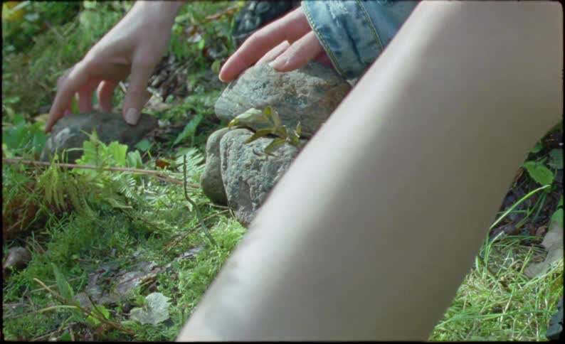 Two people sit outdoors and stack a small pile of rocks